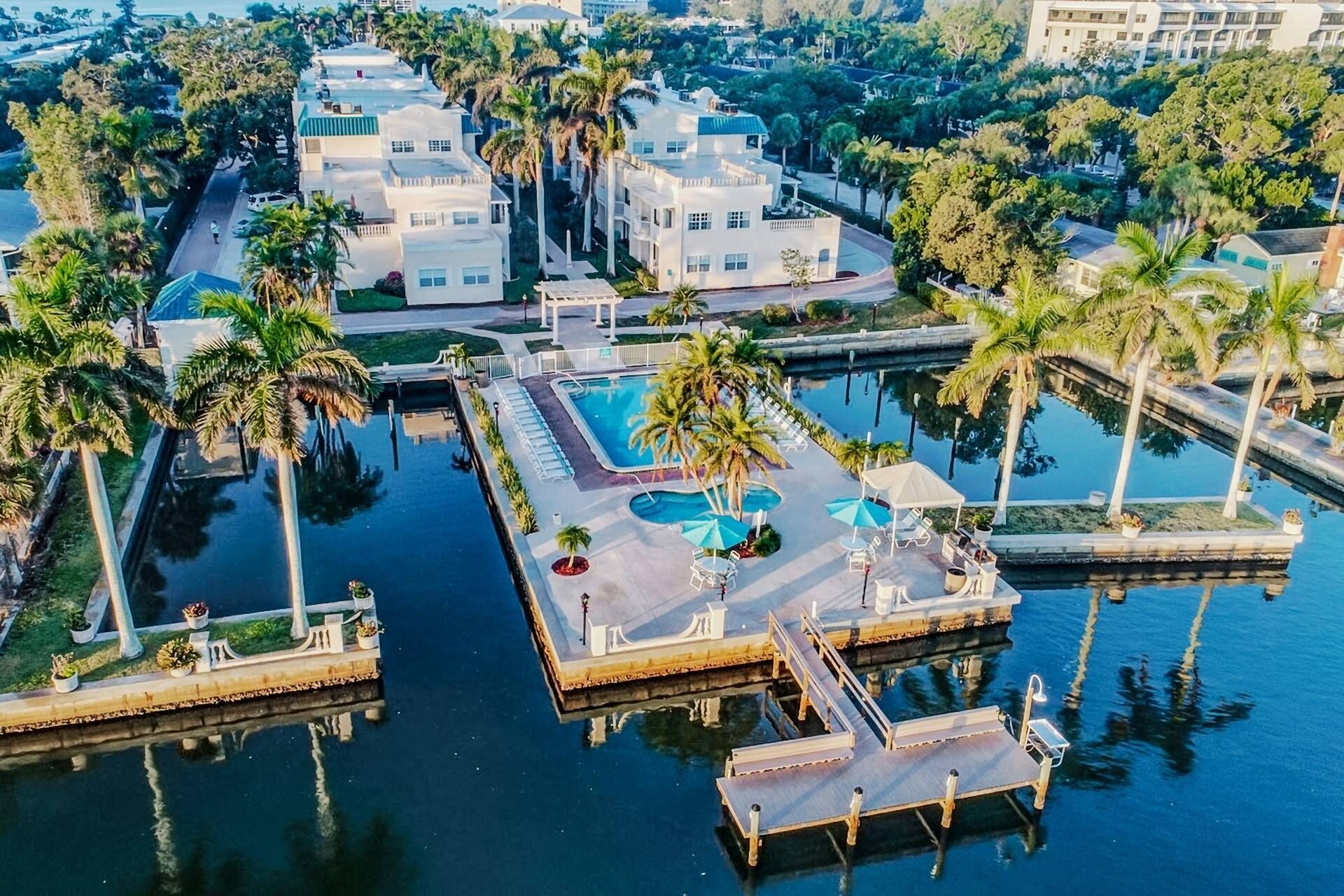 An aerial view of a resort with multiple buildings, a central pool area, and surrounding palm trees.