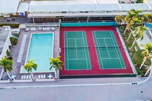 A rooftop tennis court with a pool and lounge chairs.