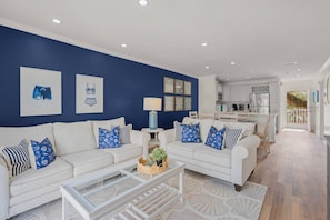 Uma sala de estar moderna com uma parede azul de destaque, sofás brancos e uma mesa de centro de vidro.