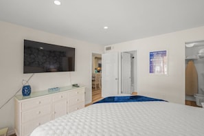 A bedroom with a bed, a dresser, a television, and a door leading to another room. - Palm Bay Club Bayside Pools Hot Tub, Private Beach (Siesta Key)