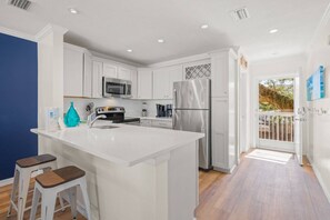 A modern kitchen with white cabinetry, stainless steel appliances, and a central island with stools.