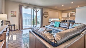 A modern living room with a leather sectional sofa, a dining area with a table and chairs, and a kitchen with white cabinets. - Modern Manson Condo w/ Pool & Lake Chelan Views! (Manson)