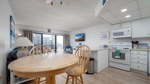 A modern kitchen with white cabinets, a microwave, and a stove. There is a dining area with a wooden table and chairs.