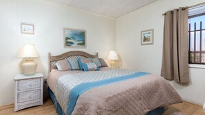 A bedroom with a bed, two bedside tables, a window with curtains, and two wall-mounted pictures.