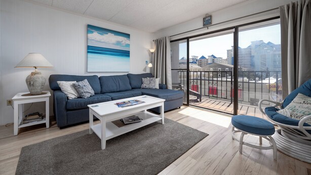 A modern living room with a blue sofa, white coffee table, and a view of the city through large windows.