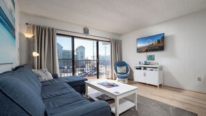 A modern living room with a grey sofa, a white coffee table, and a view of buildings through large windows.