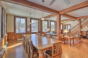 Enjoy meals in this dining area with a long table and comfortable seating, surrounded by large windows offering a view of the outdoors.