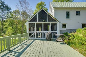 Relax on the covered deck with a bench, surrounded by lush greenery.