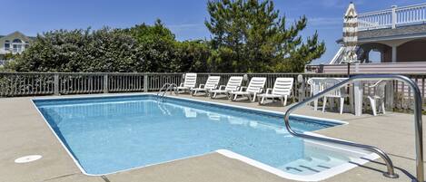 A rectangular pool with a metal ladder, surrounded by white lounge chairs and a wooden fence.