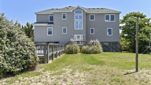 A two-story residential building with a front deck and a small garden area. - WH816- Remarkable! 6 BRs, Private Pool, Hot Tub and even a Volleyball Court! (Corolla)