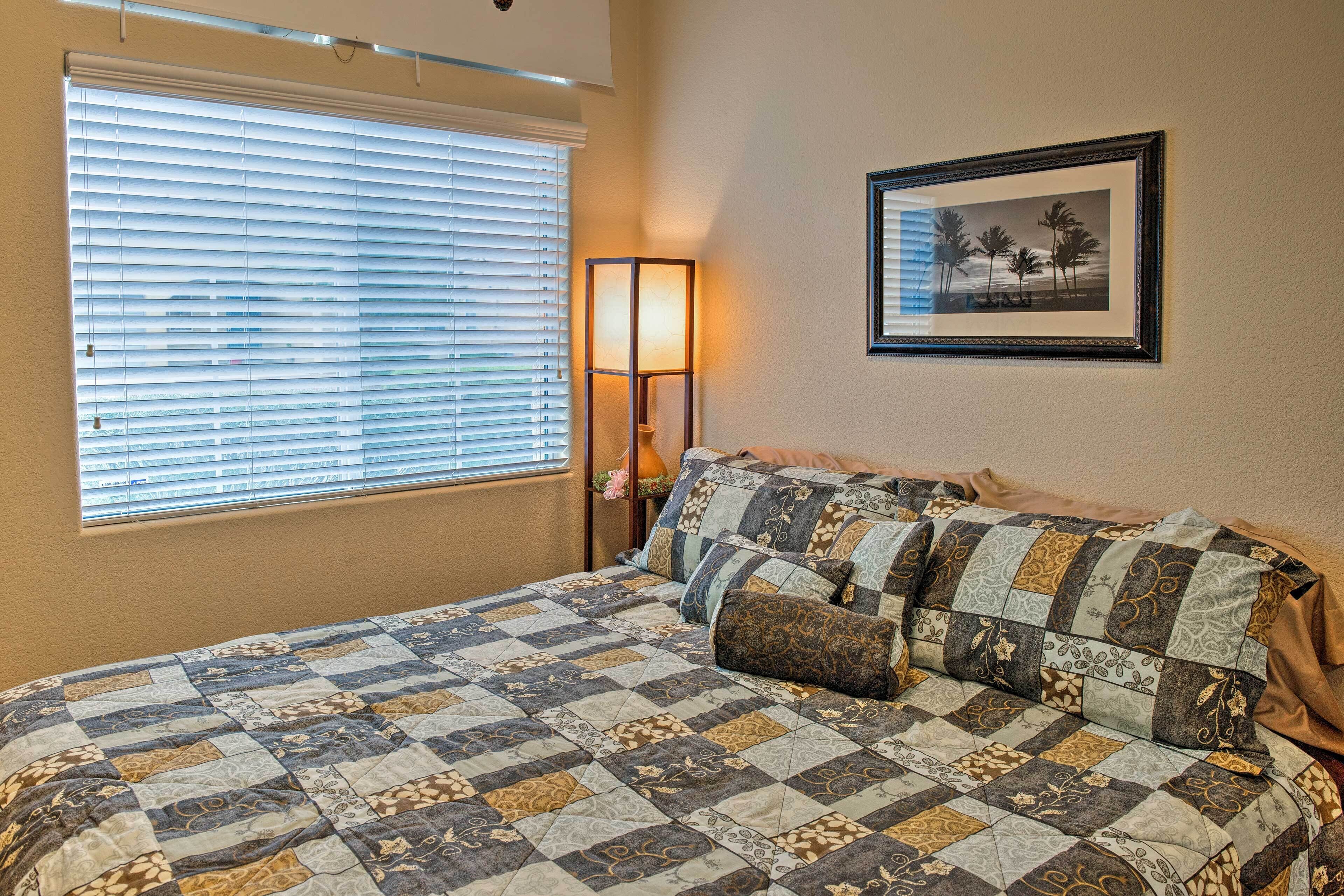 A bedroom with a large bed, a window with blinds, a bedside lamp, and a framed picture on the wall.