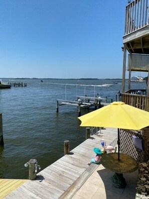 A wooden dock extending into calm waters, a yellow umbrella, and a small table with a bird fountain.