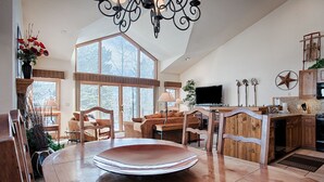 A spacious living area with a large wooden dining table, a cozy seating arrangement, a television, and a kitchen with wooden cabinets. - Quick Walk to Main St Breckenridge! Outdoor Hot Tubs/Pool! Attached Garage, Slee (Breckenridge)