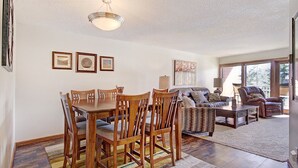 A spacious living room with a dining area, large windows, and a ceiling light fixture. - Perfect location, 2 bdrm condo, stunning views, walk to downtown, Hot tub access (Breckenridge)
