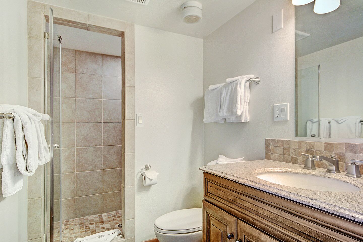 Un bagno con doccia in vetro, un water, un lavabo con mobile e uno specchio.