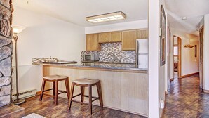 A kitchen with wooden cabinets, a tiled backsplash, a stainless steel refrigerator, and two bar stools. - Perfect location, 2 bdrm condo, stunning views, walk to downtown, Hot tub access (Breckenridge)