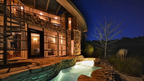 Ein modernes Haus mit Natursteinfassade, einem Swimmingpool und einem gut beleuchteten Außenbereich.