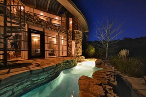 Une maison moderne avec une façade en pierre, une piscine et un espace extérieur bien éclairé.