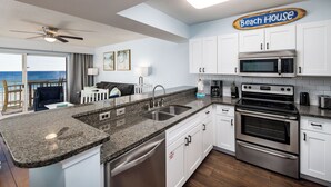 A kitchen with white cabinets, a granite countertop, stainless steel appliances, and a sign reading "Beach House". - PI 311: Ocean’s Embrace - Amazing! Granite, 4Led Tvs, Reserved Parking (Fort Walton Beach)
