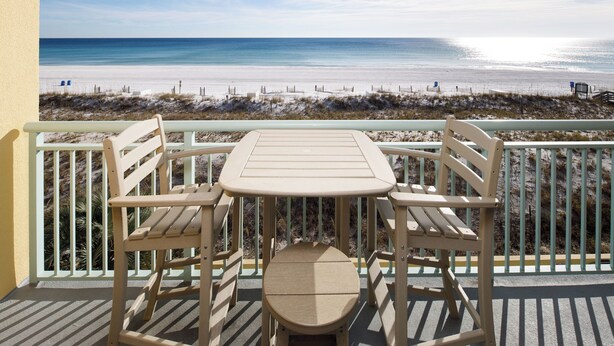 A balcony with a table and chairs overlooking a beach. - PI 311: Ocean’s Embrace - Amazing! Granite, 4Led Tvs, Reserved Parking (Fort Walton Beach)