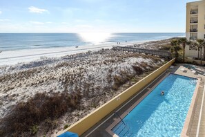 A pool adjacent to a beach with a wooden walkway leading to the shore.