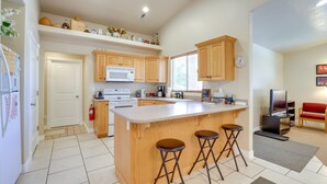 A modern kitchen with a central island, wooden cabinets, a microwave, and a television in the corner. - Family-Friendly Utah Home, Easy Access to Zion! (La Verkin)