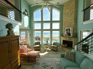A spacious living room with a large bay window overlooking the beach, a fireplace, and a staircase. - KH5205- Oceanfront, 4 BRs (2 Masters), Hot Tub & Outstanding Ocean Views! (Kitty Hawk)