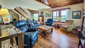 Ein geräumiges Wohnzimmer mit hohen Decken, Holzdielen und einer Treppe, die in ein Obergeschoss führt.