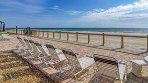 Un salon de plage doté de chaises longues et d’une rambarde en bois donnant sur l’océan.