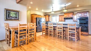 A spacious kitchen with wooden cabinets, a central island, and a dining area with chairs. - Rustic Bryce Canyon Home w/ Deck on Sevier River! (Hatch)
