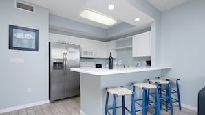 A modern kitchen with a central island, bar stools, stainless steel appliances, and a light blue color scheme.