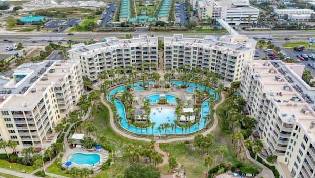 A multi-story hotel with a central swimming pool surrounded by palm trees and smaller pools.