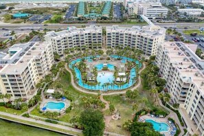 Un hotel a più piani con una piscina centrale circondata da palme e piscine più piccole.
