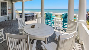 A covered outdoor area with a view of the ocean, featuring a round table and chairs, and a hot tub.