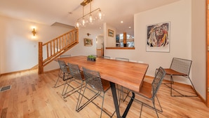 A spacious dining area with a long wooden table and wireframe chairs, a wooden staircase, and a modern chandelier. - Wind River 3: Teton Village-Walk to Ski/Lift Sleeps 10- Pool / Hot Tub Access (Teton Village)