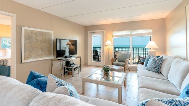 Una sala de estar con sofá, mesa de centro, televisor y un balcón con vista al mar.