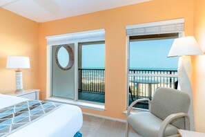 Ein Hotelzimmer mit Bett, Sessel, Tisch, Lampe und Meerblick vom Balkon.
