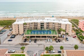 Ein mehrstöckiges Hotel mit Dachterrasse, Tennisplatz, Parkbereich und Blick auf den Strand.