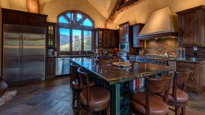 A spacious kitchen with a large island, wooden beams, and a view of mountains through a large window.