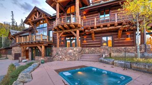 A log cabin with a hot tub, stone steps, and a balcony.