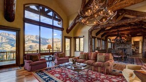 A spacious living room with large windows, a fireplace, and a chandelier.