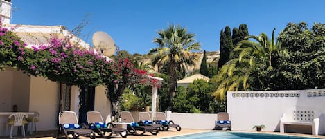 A pool area with lounge chairs, a white wall, and a satellite dish.