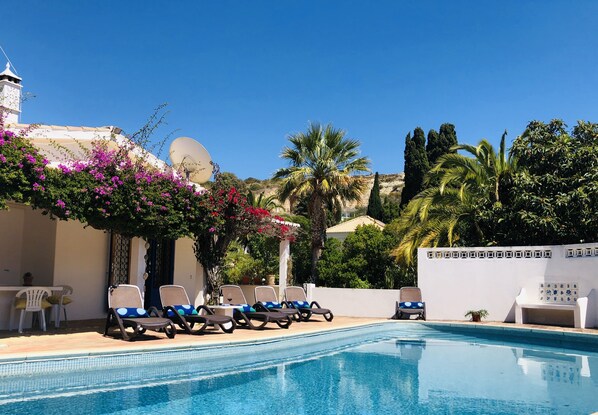 A pool area with lounge chairs, a white wall, and a satellite dish.