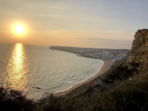 A coastal landscape with a beach, cliffs, and a city in the distance.