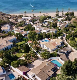 A residential area with houses, a swimming pool, and a beach in the background.
