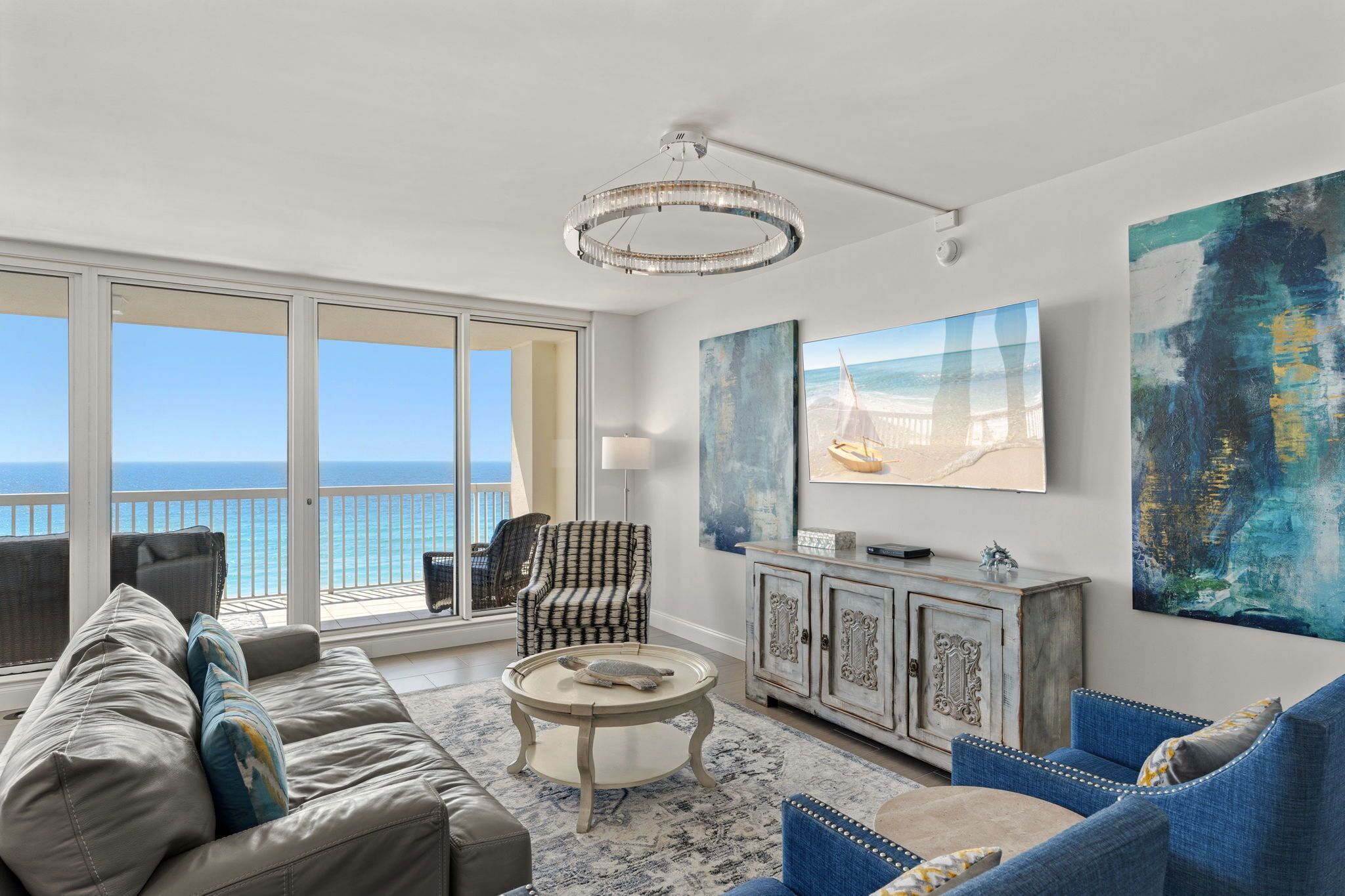 A spacious living room with a large window overlooking the ocean, a chandelier, and a modern fireplace.