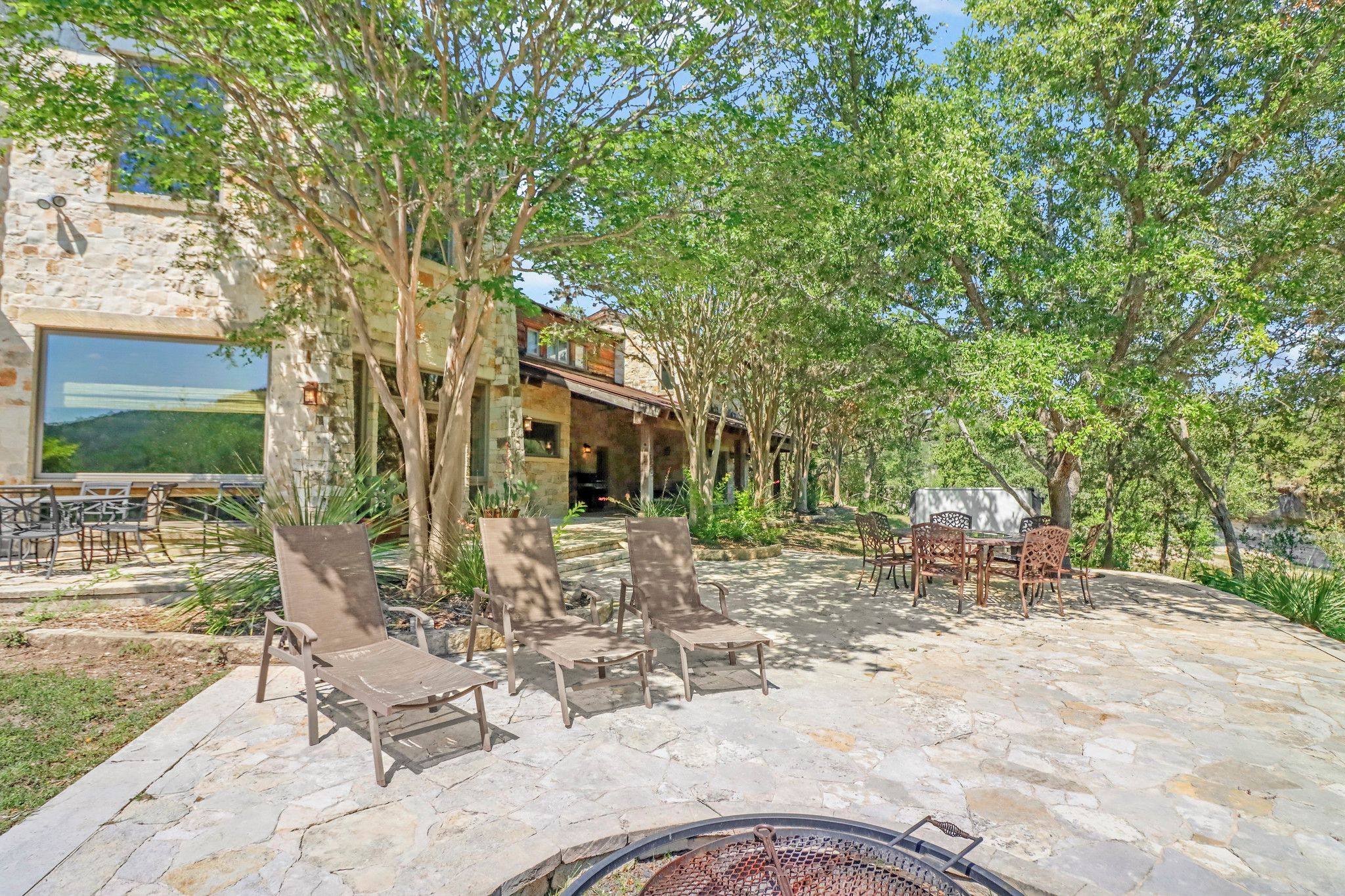 An outdoor patio with stone flooring, lounge chairs, and a grill area.