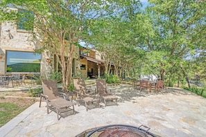 An outdoor patio with stone flooring, lounge chairs, and a grill area.