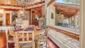 A spacious dining area with a wooden table and chairs, a stone wall, and a view of the outdoors.
