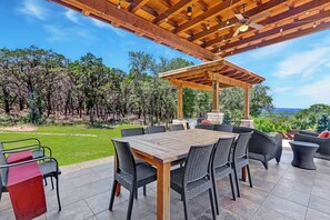 Un patio al aire libre con una pérgola de madera, una mesa de comedor con sillas y vistas a una zona boscosa.